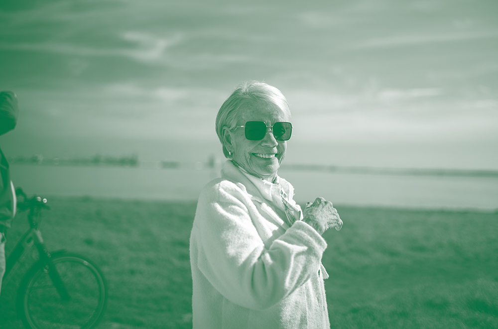 Oudere vrouw met zonnebril lacht aan de kust