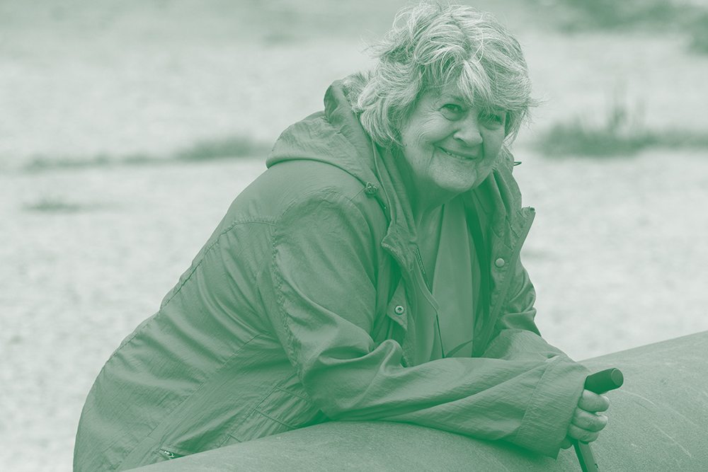 Vrolijke oudere vrouw met wandelstok aan zee